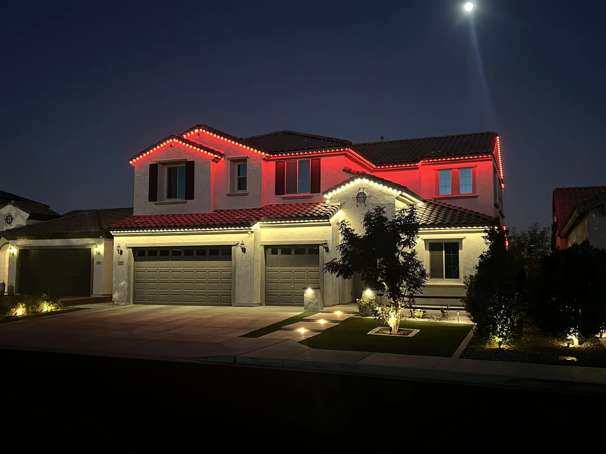 Red lighting on the upper roofline and warm-white lighting below on an Arizona home.