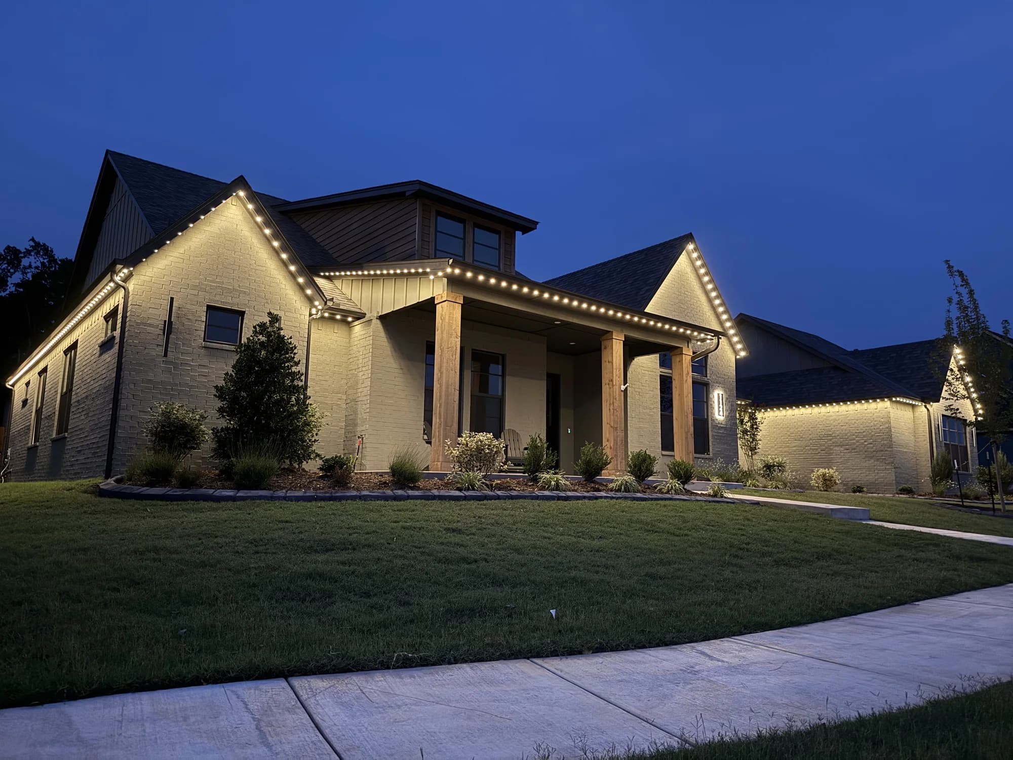 Warm-white TruLight roofline lights on a pale stone home in Oklahoma at dusk.