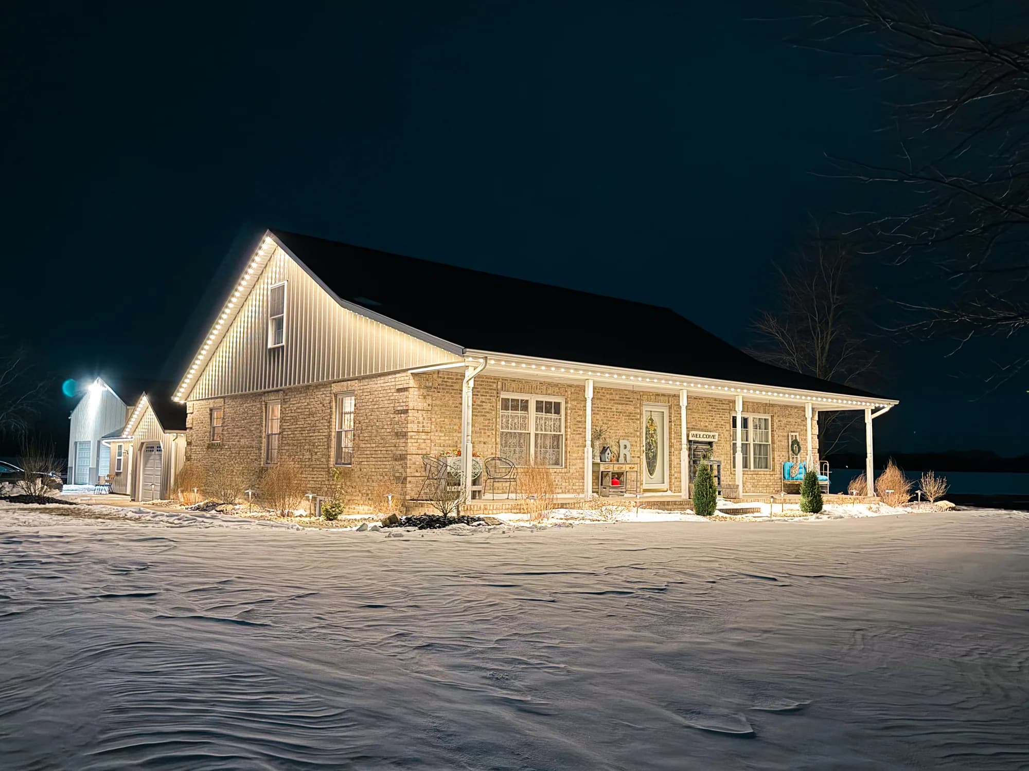 White TruLight roofline lighting on a brick home with a long porch and snow-covered yard.